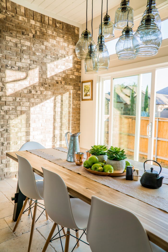 get-in-touch Sunlit dining room with contemporary decor and a rustic brick wall, featuring stylish lighting and a wooden table.