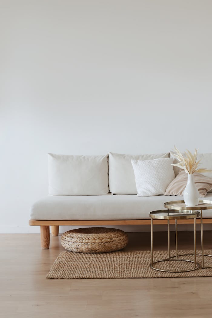 services-03 A chic minimalist living room featuring a white sofa with cushions, dried flowers in a vase, and a wooden floor.